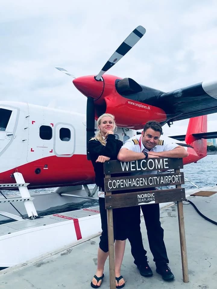 Two crew members by a 'Welcome to Copenhagen City Airport' sign in front of the floatplane