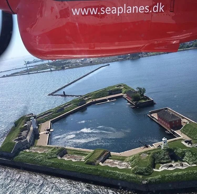 A sea fort in Copenhagen harbour seen from under the red wing of a Twin Otter