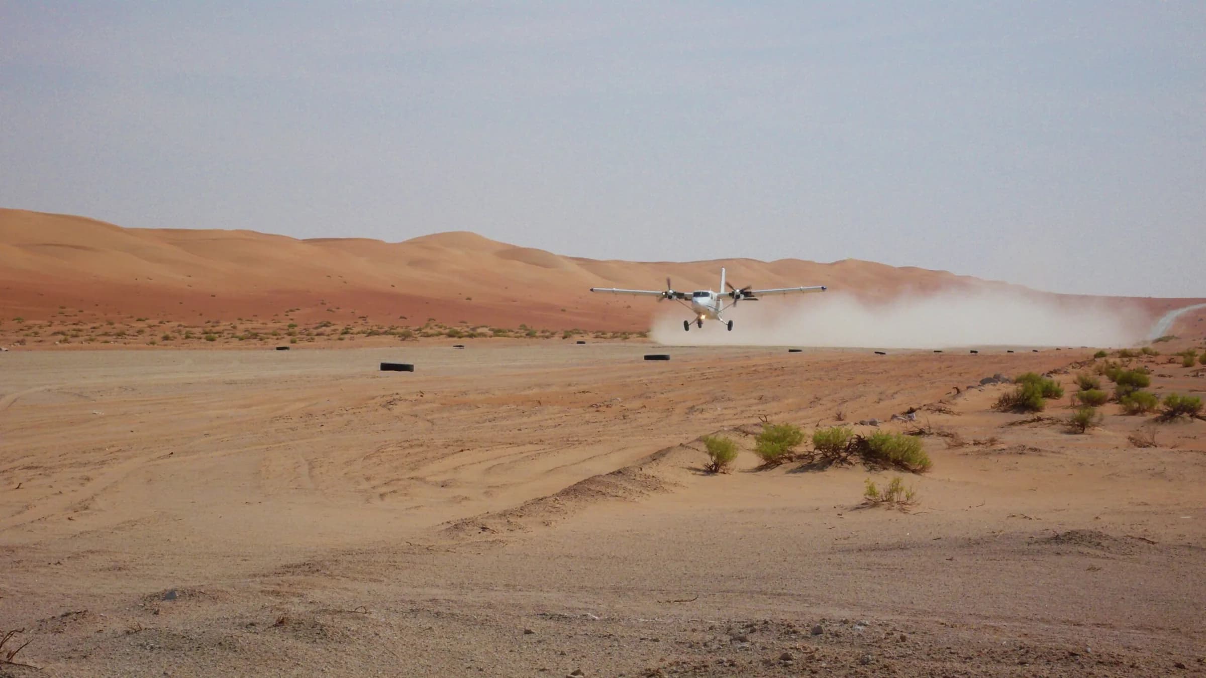 A Twin Otter taking off from a desert strip in a cloud of dust.