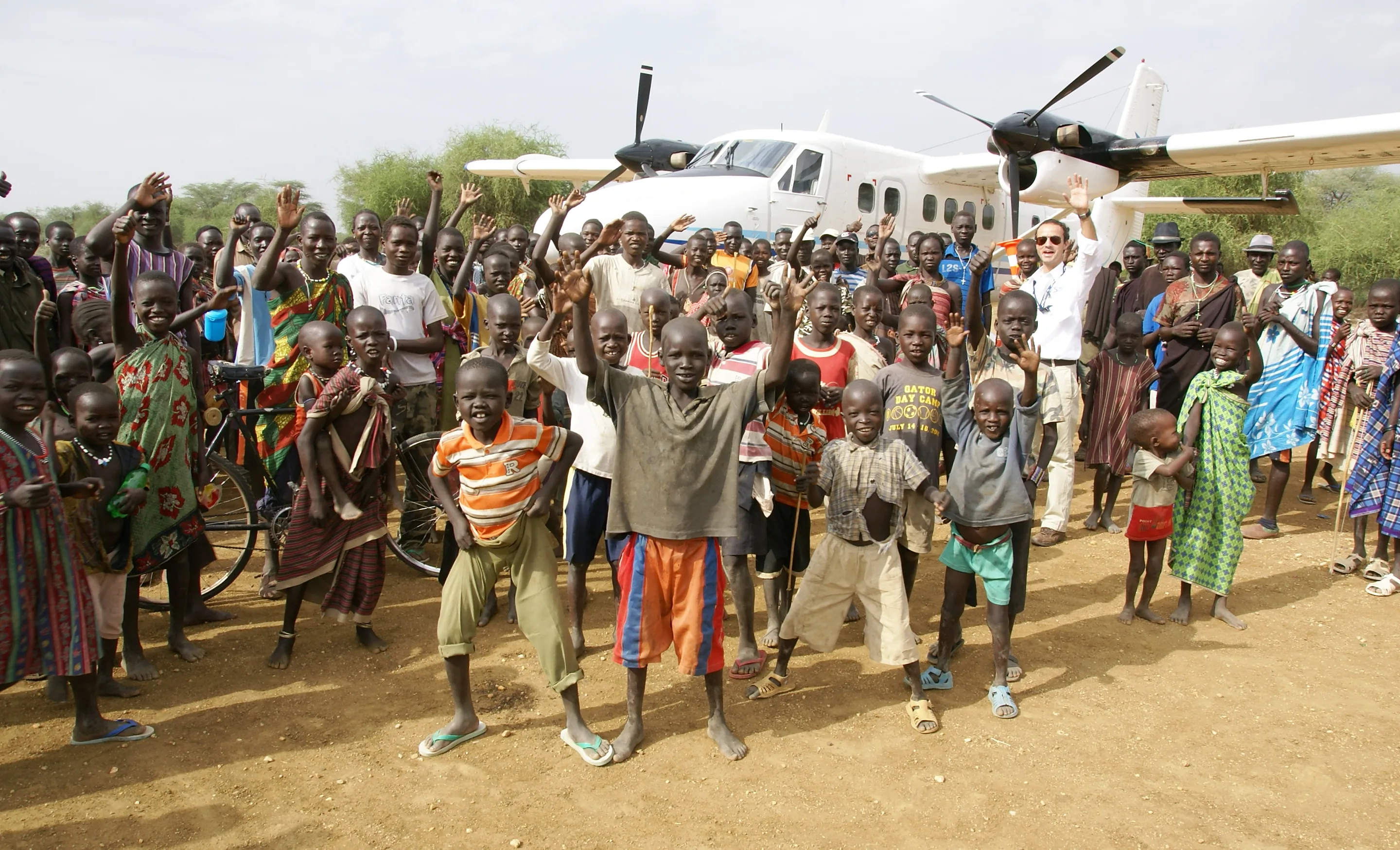A crowd waving in front of a Zimex Twin Otter on a dirt strip in South Sudan